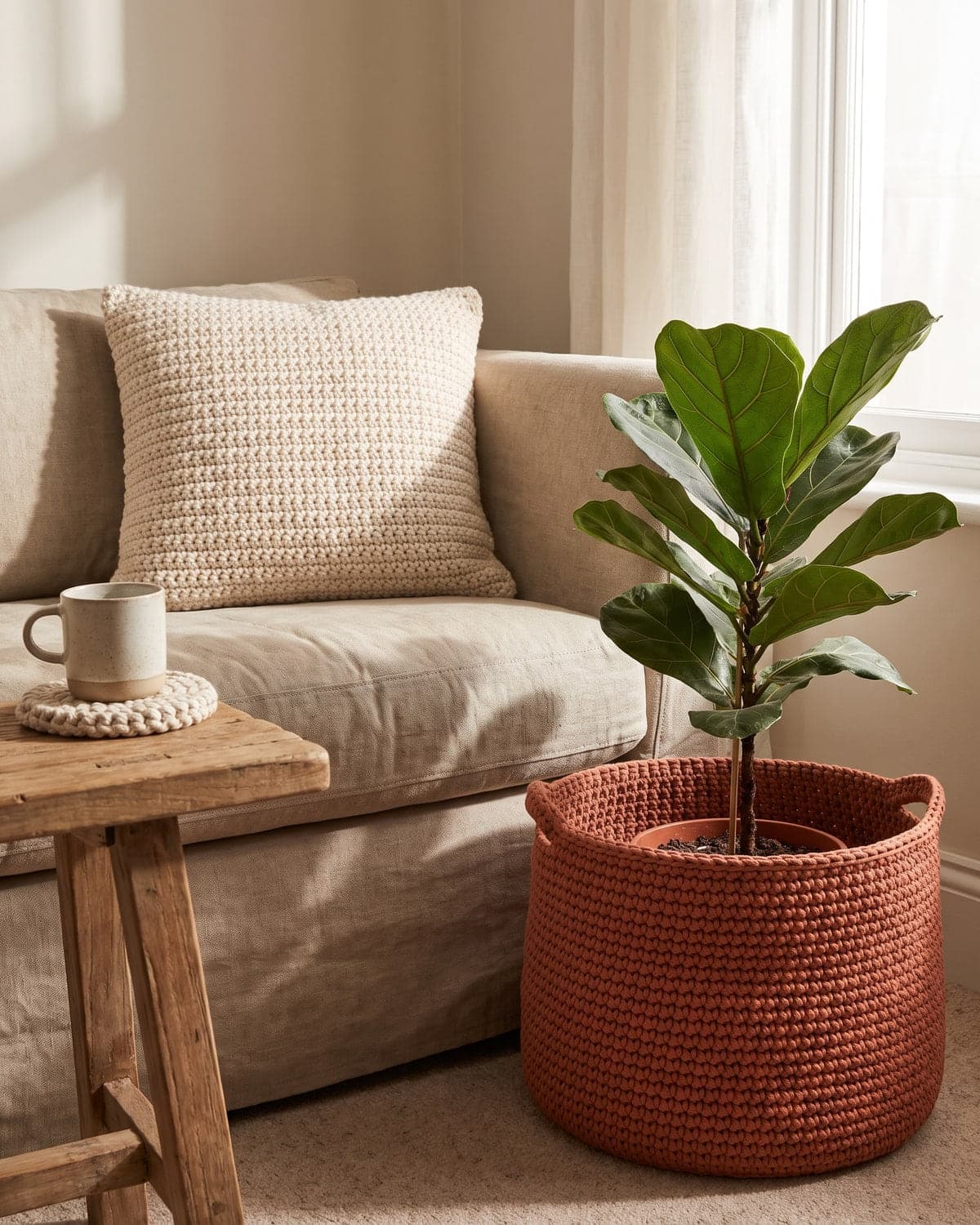 Sofa corner with a crochet cushion, a terracotta crochet basket holding a plant and a crochet coaster