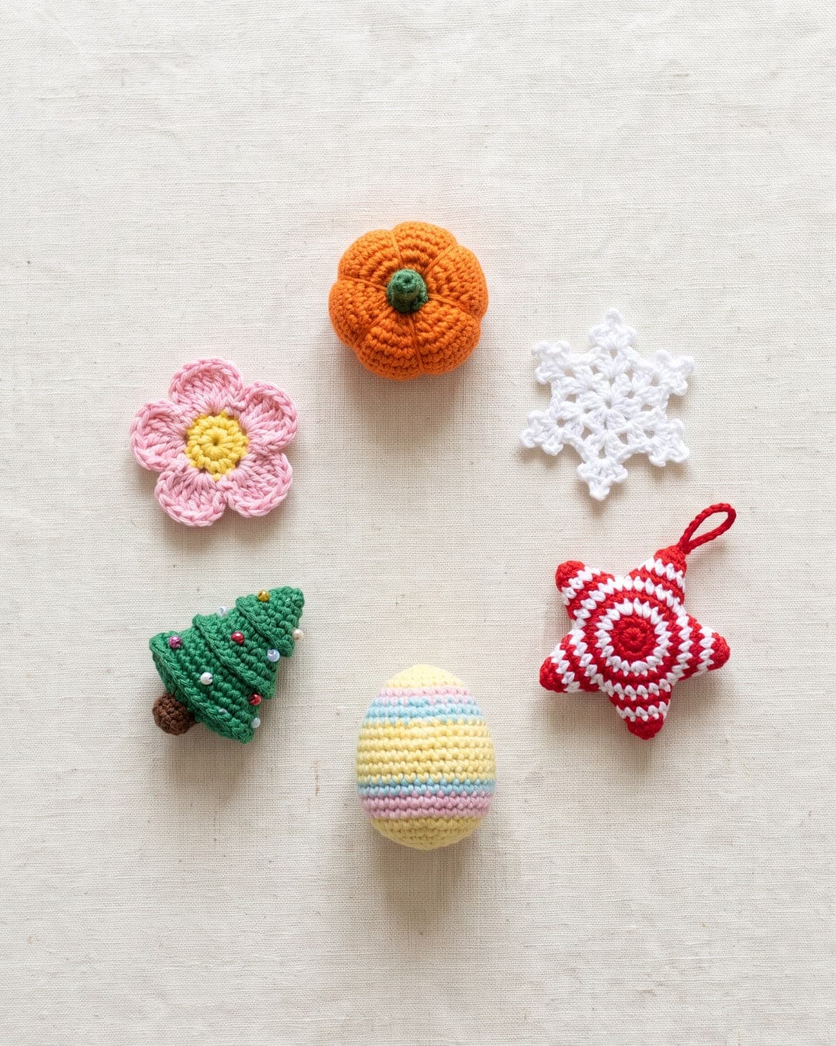 Small crochet pumpkin, snowflake, star, Easter egg, Christmas tree and flower on linen