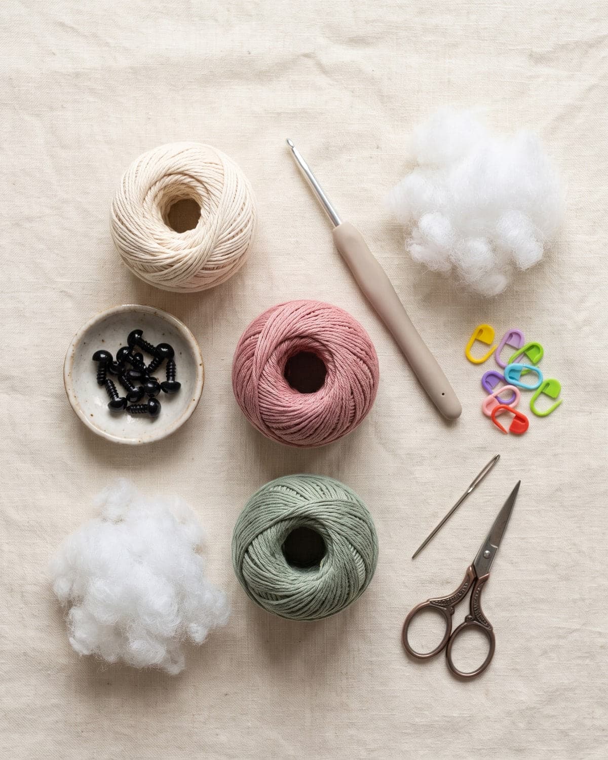 Cotton yarn, a small crochet hook, safety eyes, stuffing, stitch markers, a needle and scissors on linen