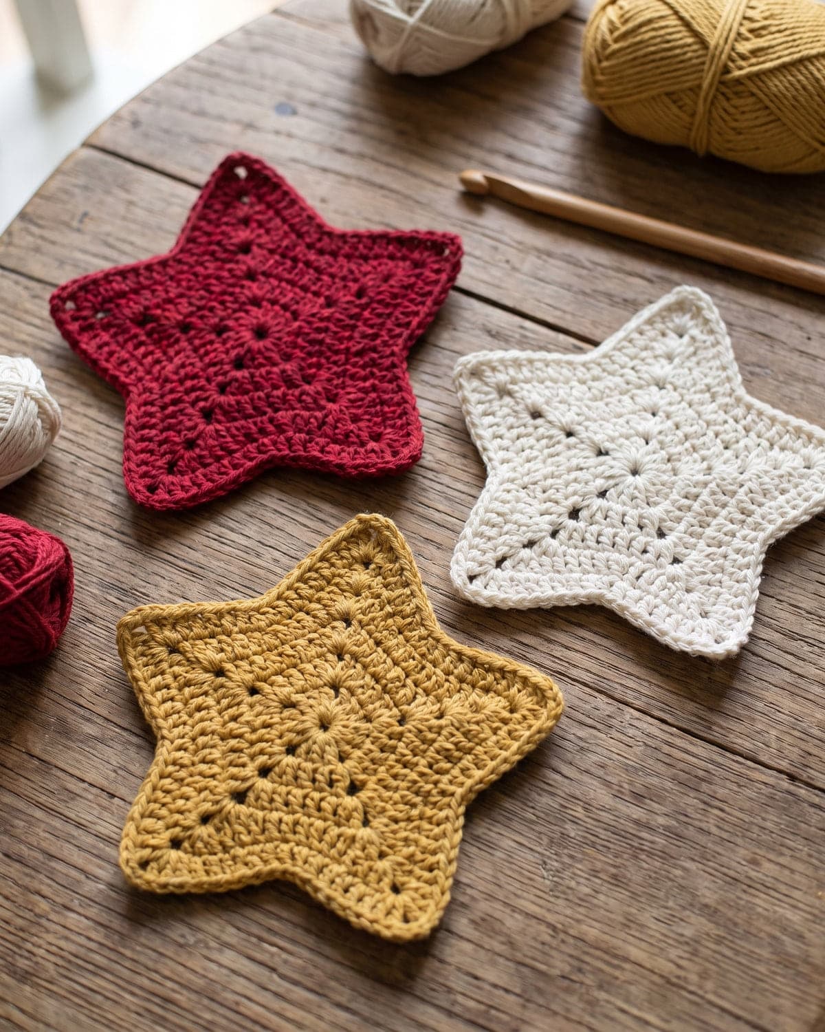 Three flat crochet five-point stars in red, white and mustard on a wooden table