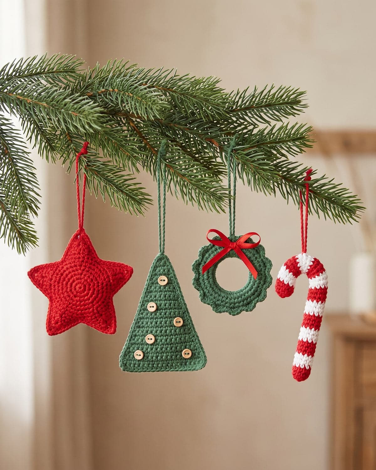 Crochet Christmas ornaments on a fir branch: a red star, a green tree with buttons, a wreath with a red bow and a striped candy cane