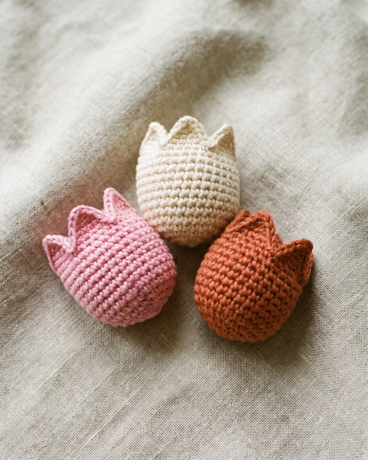 Three small crochet tulip heads in pink, cream and terracotta on a linen cloth