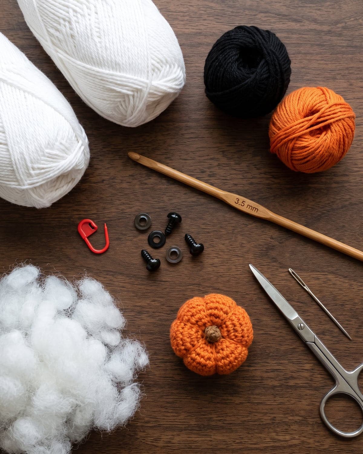 White, black and orange yarn with a crochet hook, safety eyes, stuffing, a stitch marker and scissors on dark wood