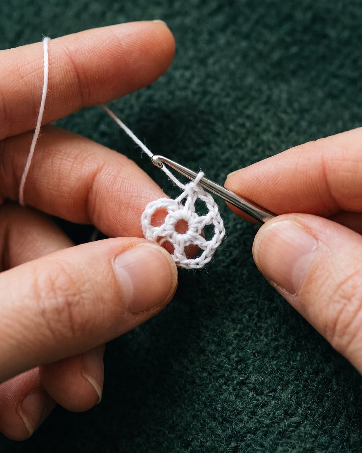 Fingers holding the small centre of a white crochet snowflake with a ring of chain loops and a steel hook