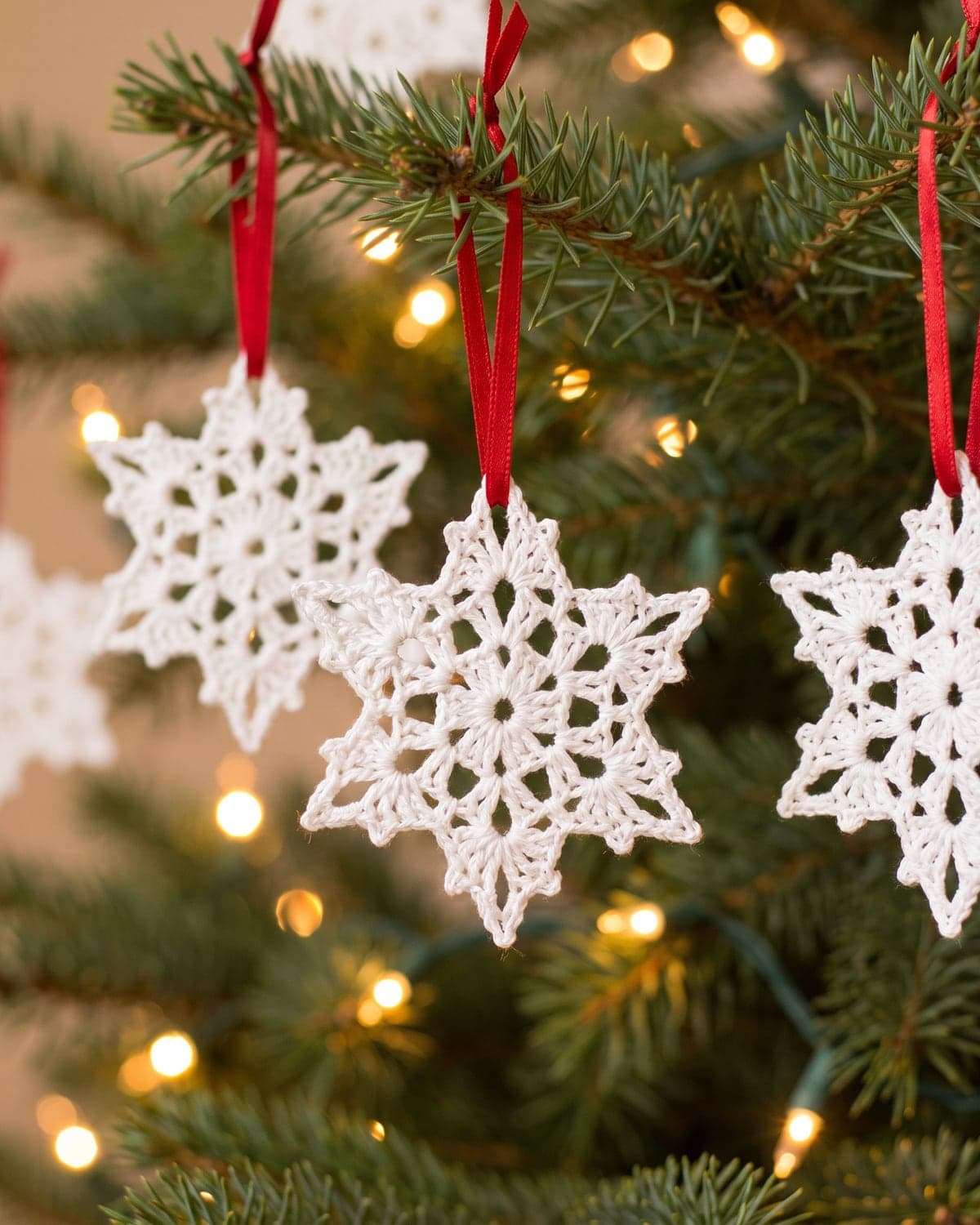 White crochet snowflakes hanging on red ribbons from a Christmas tree branch with warm lights