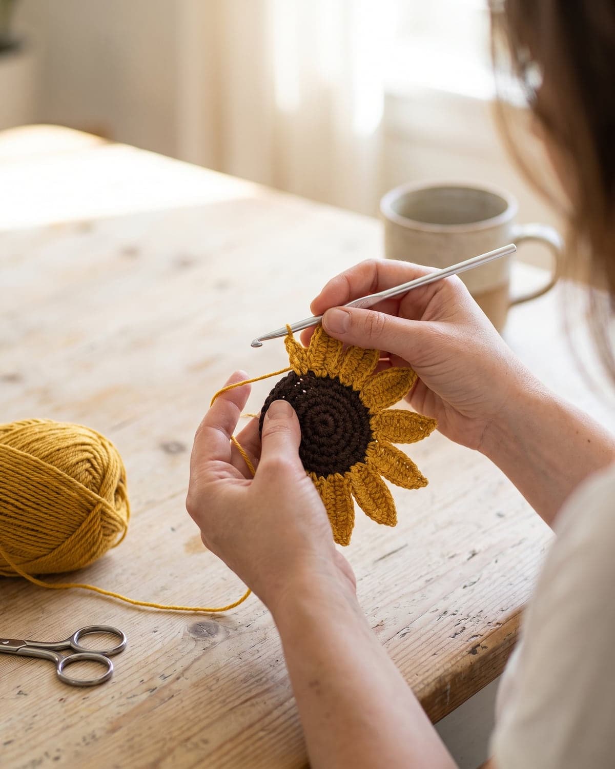 Hands crocheting yellow pointed petals around the brown centre of a crochet sunflower