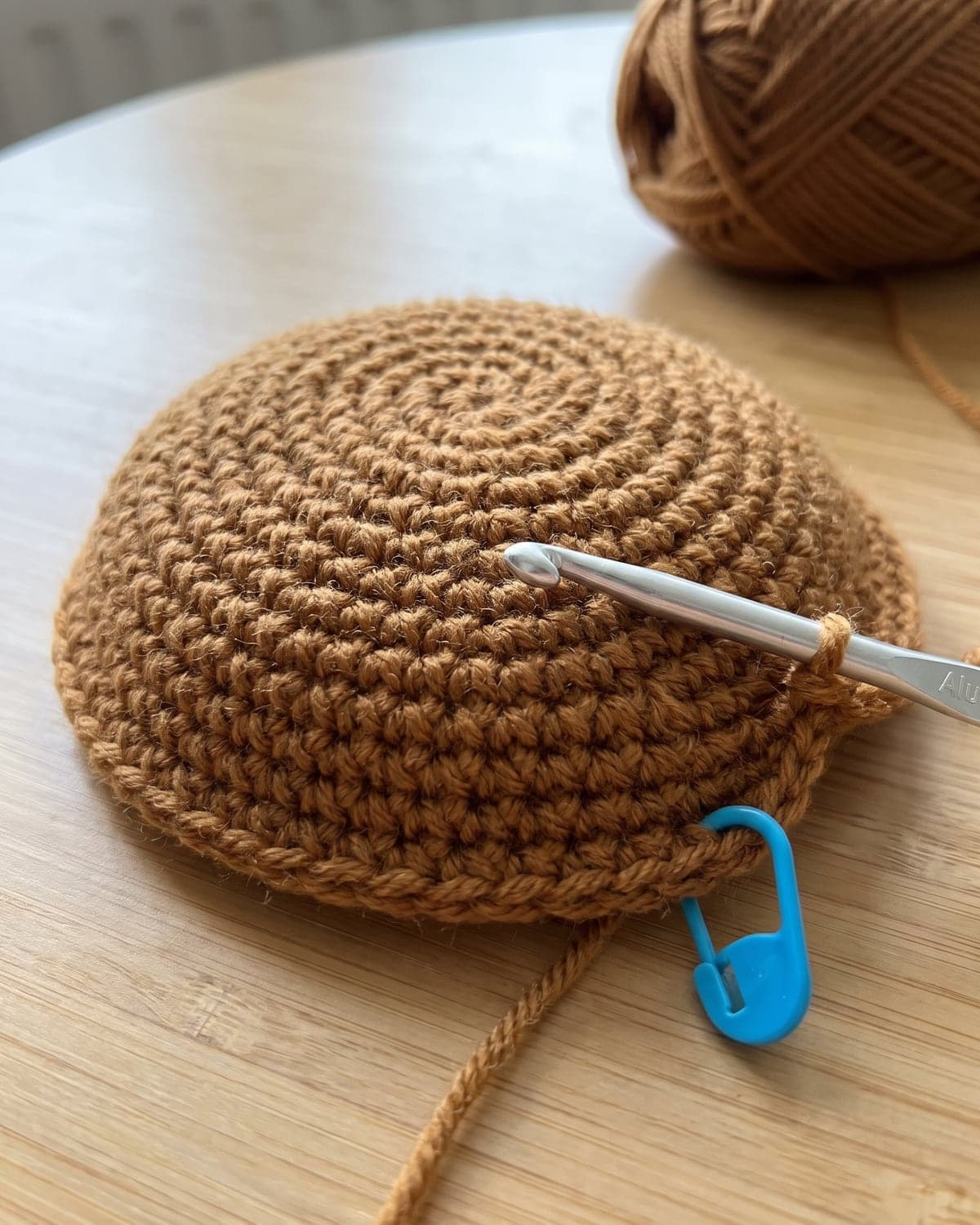 Caramel brown crochet dome for a turtle shell with a hook in the loop and a blue stitch marker