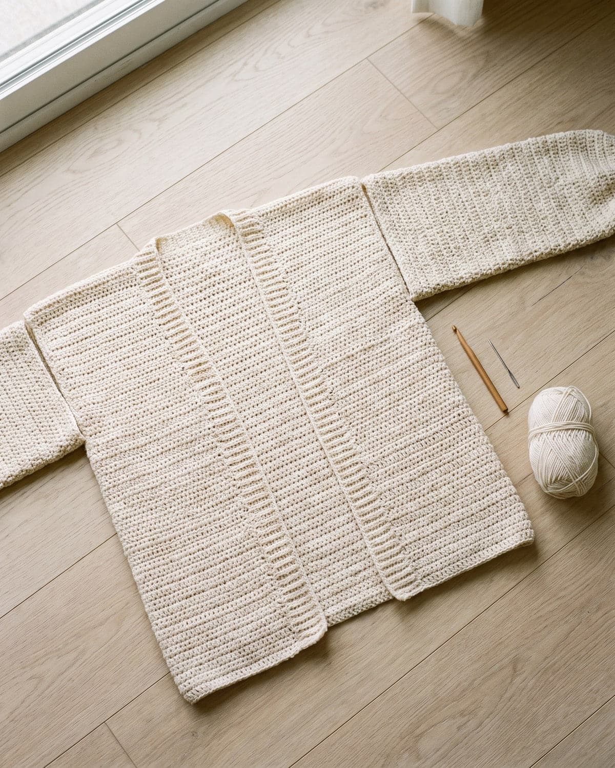 Cream crochet cardigan laid flat on a wooden floor with its sleeves outstretched