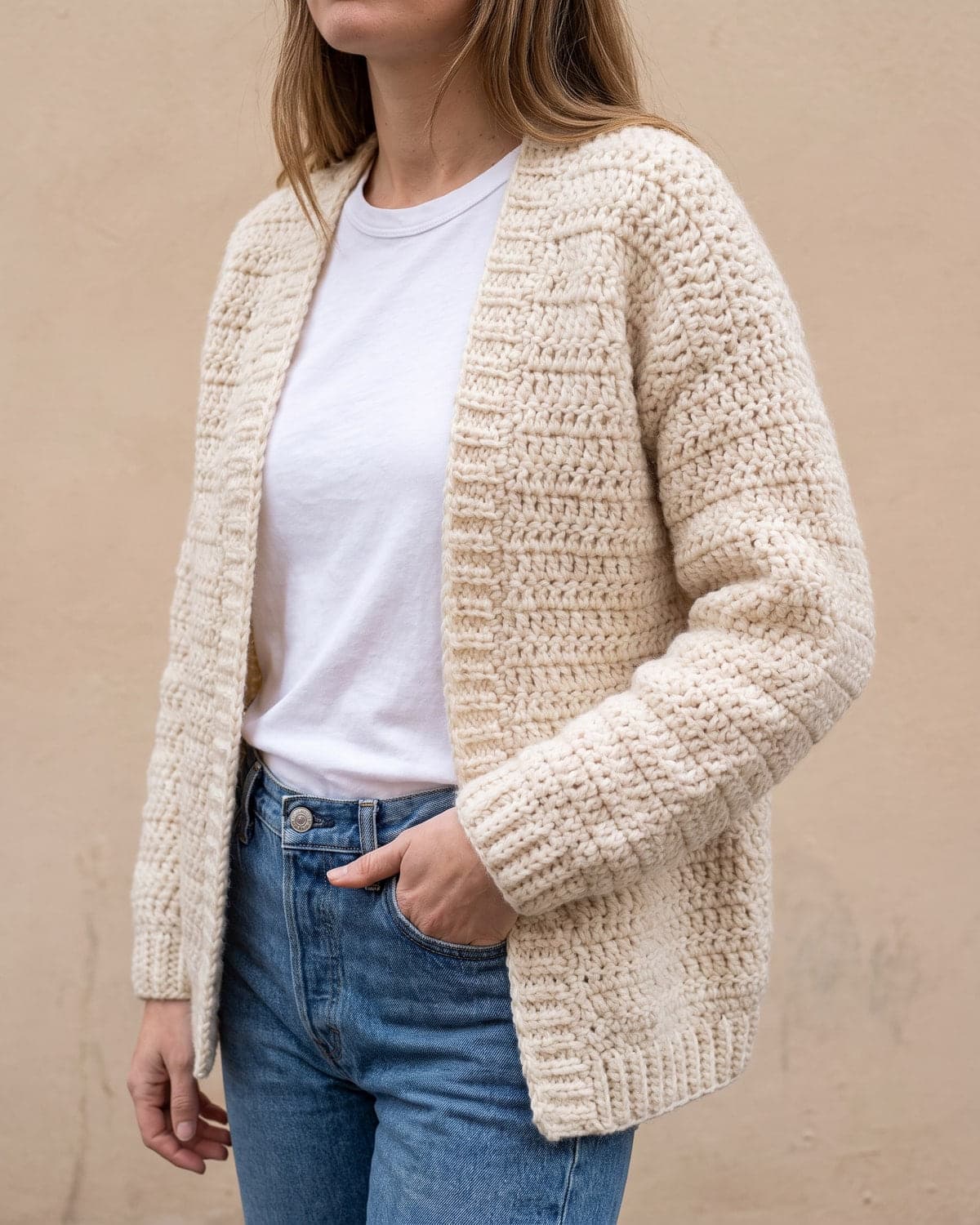 Woman wearing an open-front cream crochet cardigan over a white t-shirt and jeans
