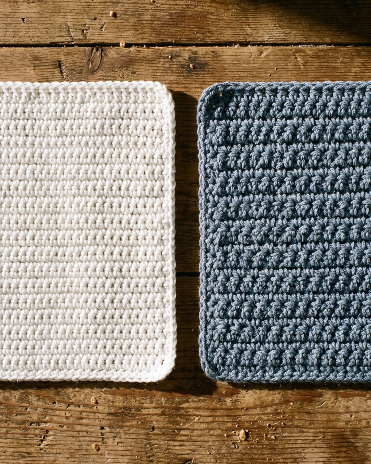 Smooth white crochet dishcloth beside a textured blue-grey crochet dishcloth on dark wood