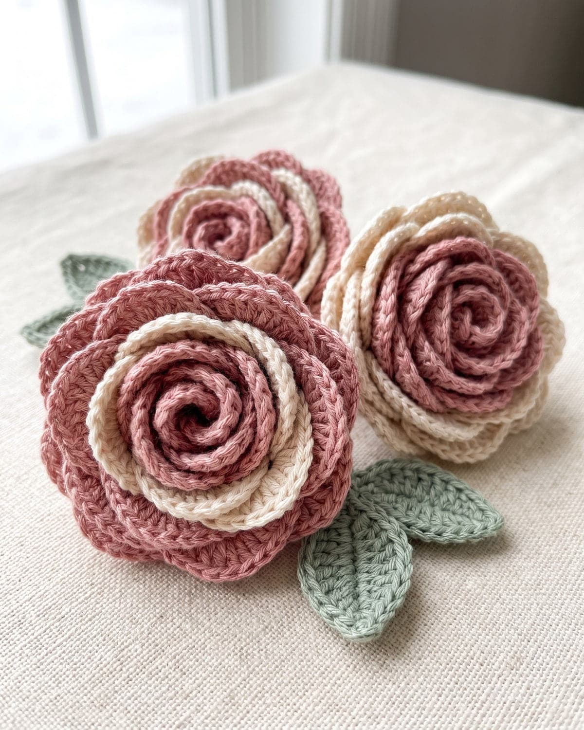 Three rolled crochet roses in dusty pink and cream with sage green crochet leaves