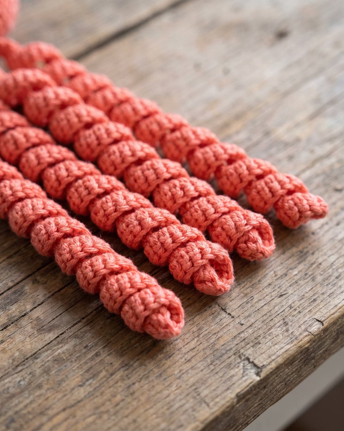 Close-up of four curly crochet spiral tentacles in coral yarn on a wooden table