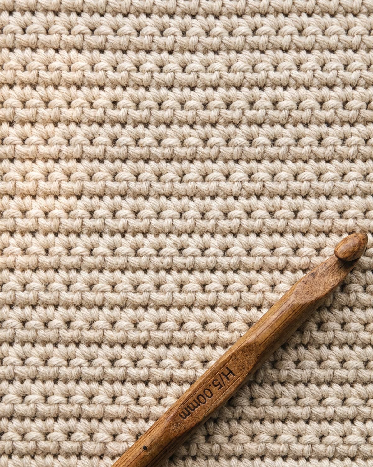 Close-up of dense cream crochet fabric with a wooden crochet hook resting on it