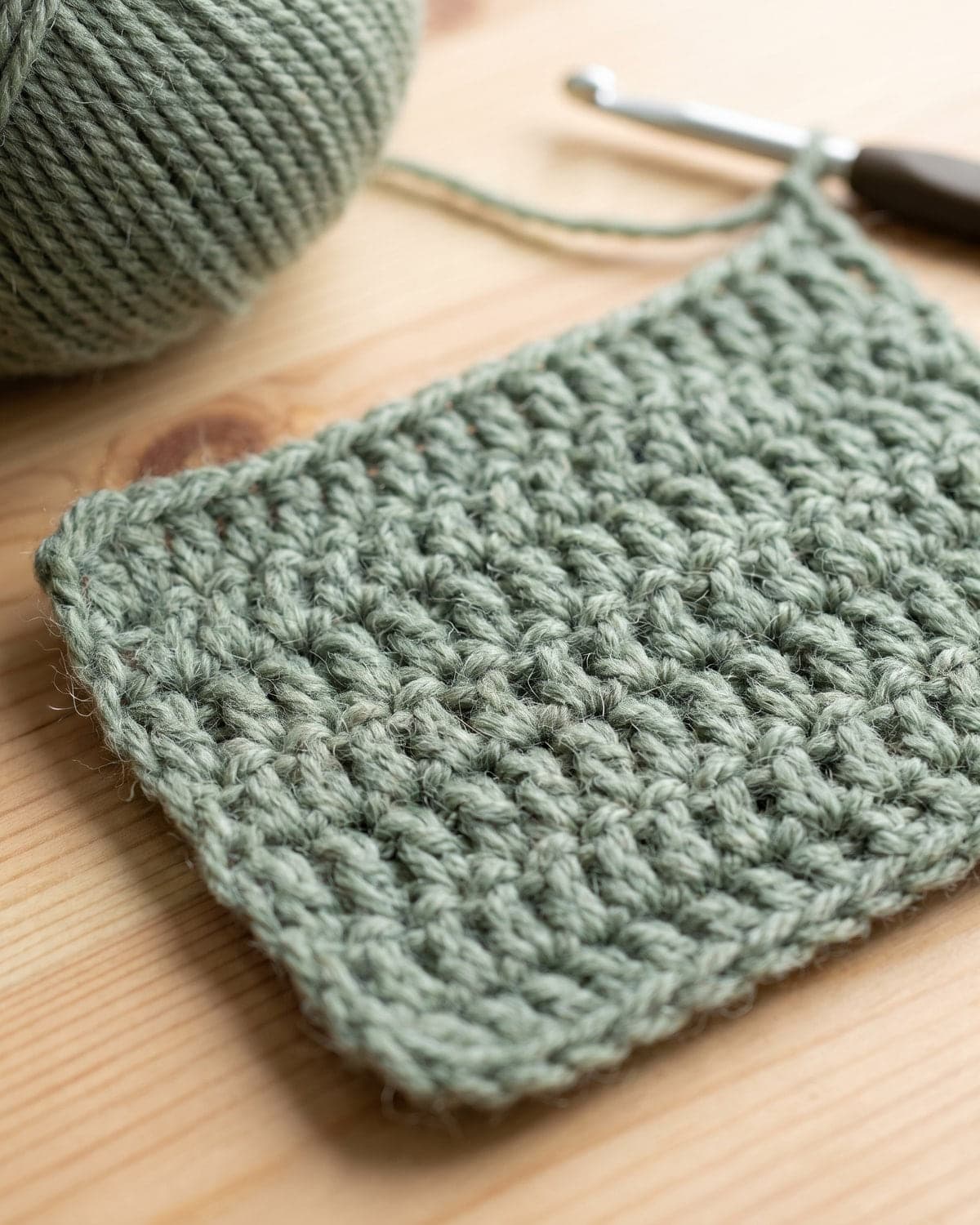 Sage green crochet swatch with soft medium-height stitches beside a ball of yarn