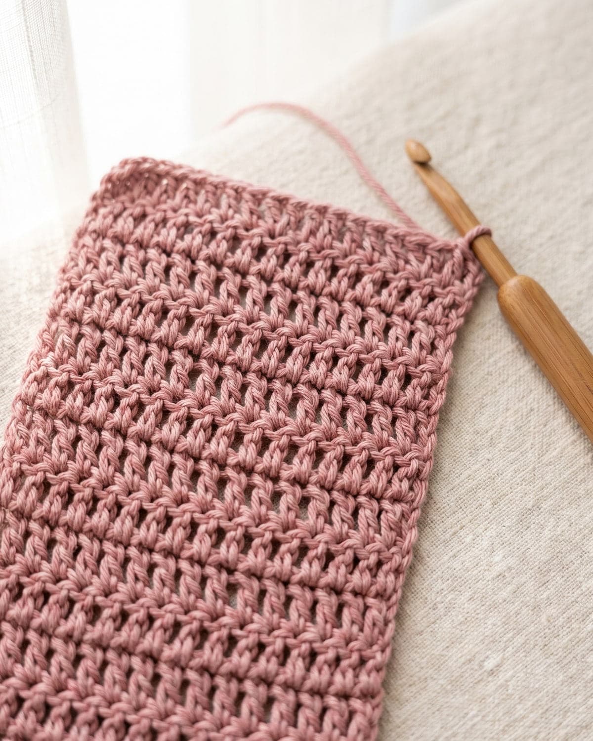 Dusty pink crochet swatch made of tall open stitches with a bamboo hook beside it