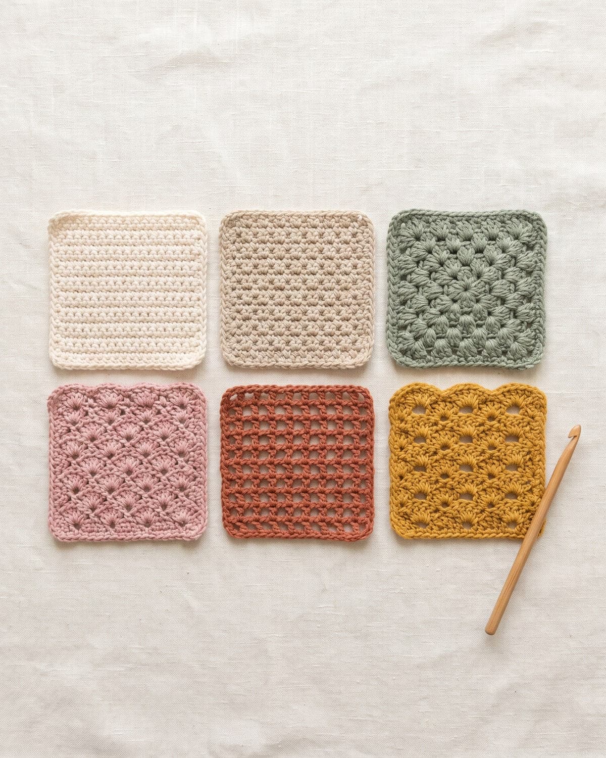 Six square crochet swatches in different stitches and muted colours laid out in a grid with a wooden hook