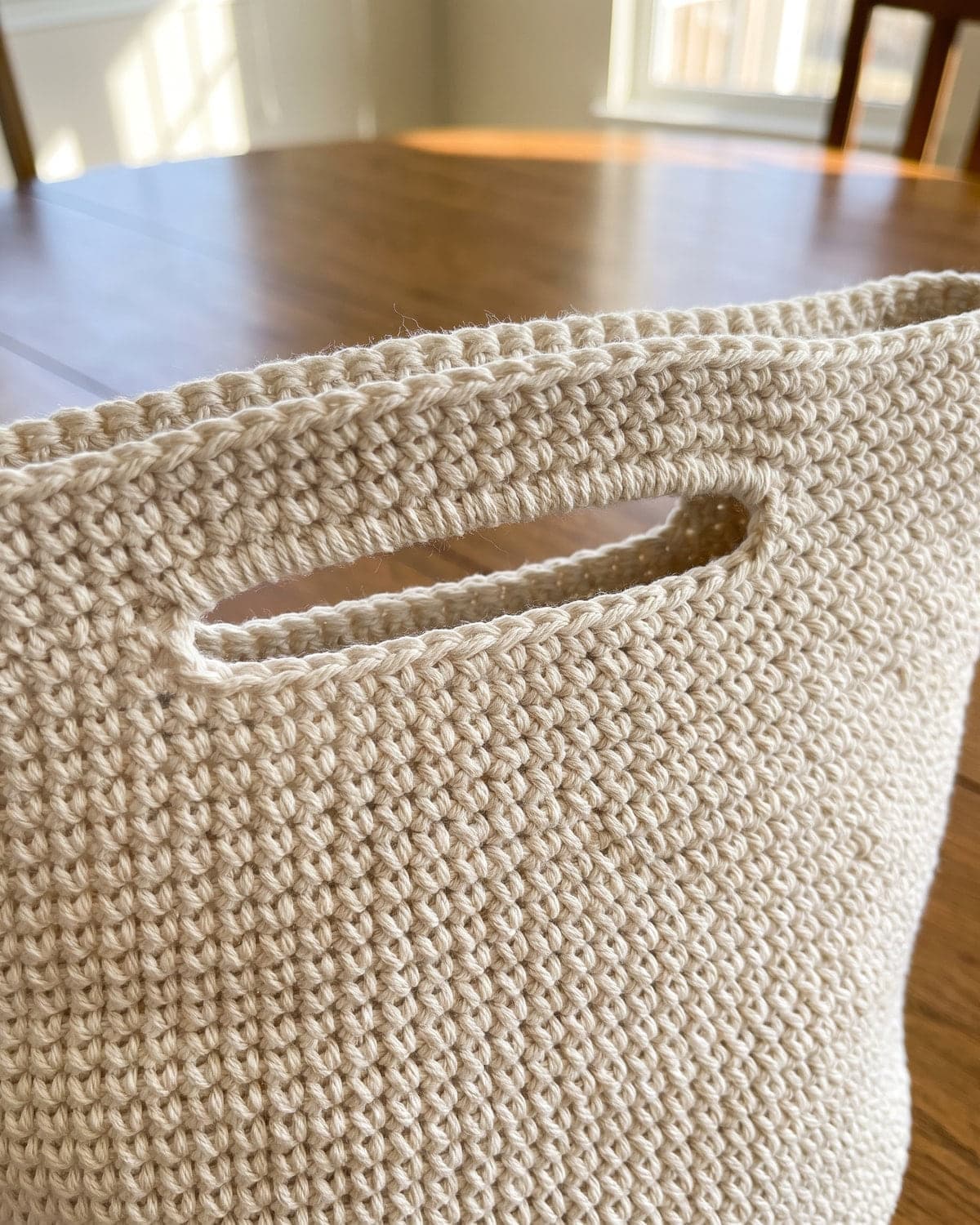 Close-up of a built-in handle opening near the top of a cream crochet tote bag