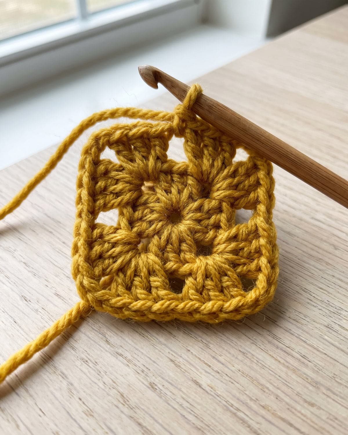 Small mustard granny square just started, with a wooden crochet hook in the working loop
