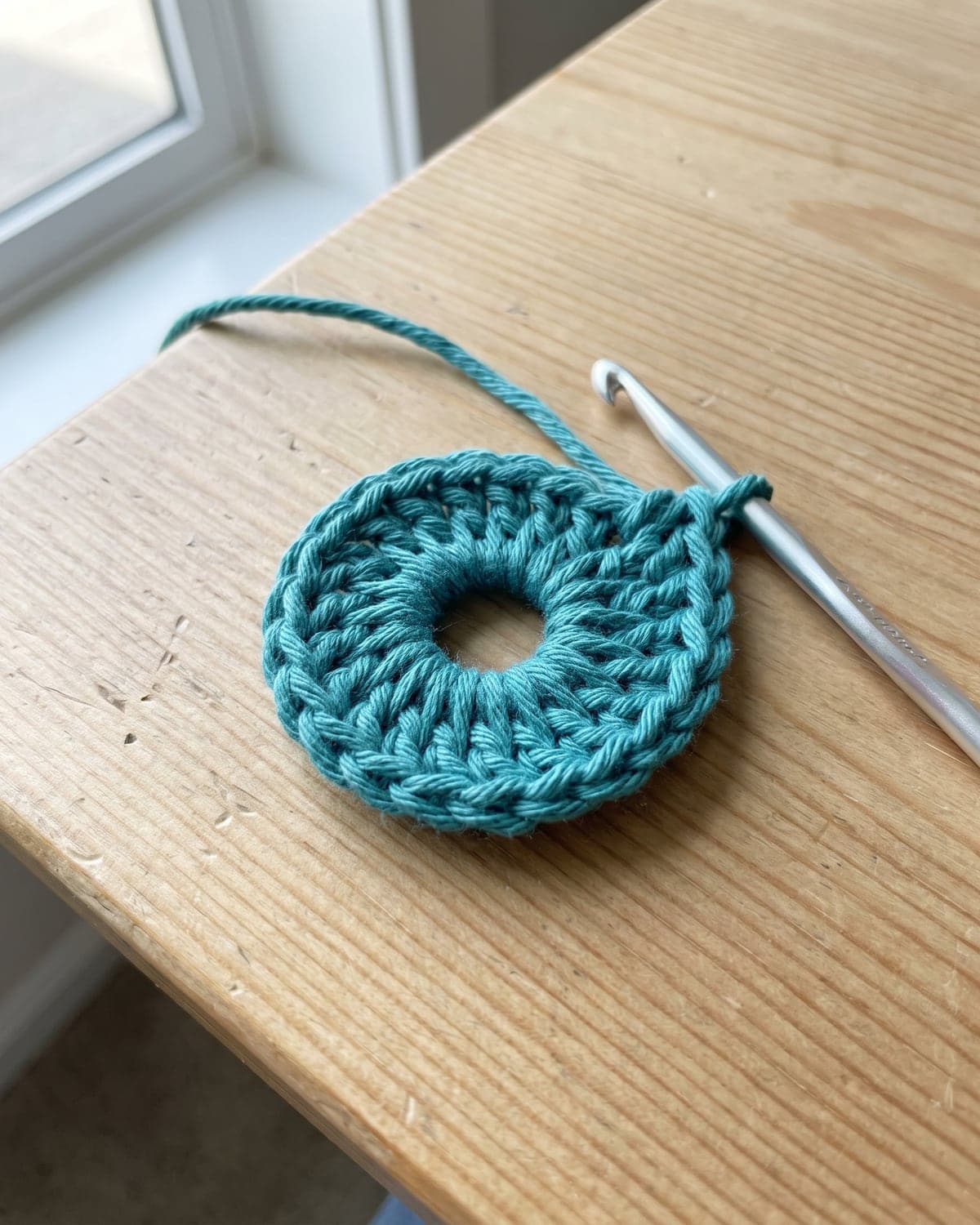 Small teal crochet ring with an open hole in the centre and a hook in the last loop, before the tail is pulled