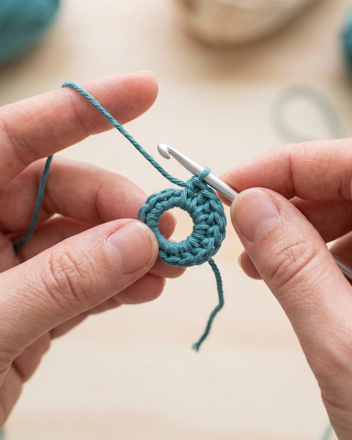Hands holding a teal crochet magic ring with the first round of stitches and a crochet hook in the loop