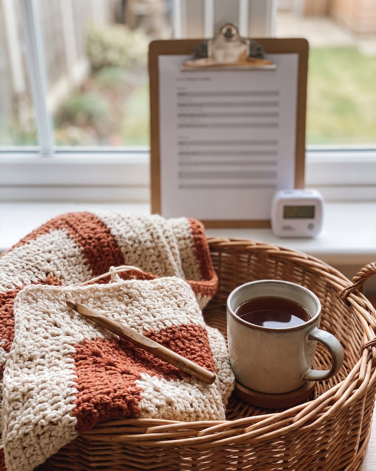 Cream and terracotta crochet project in a basket with a cup of tea, a pattern on a clipboard and a row counter behind