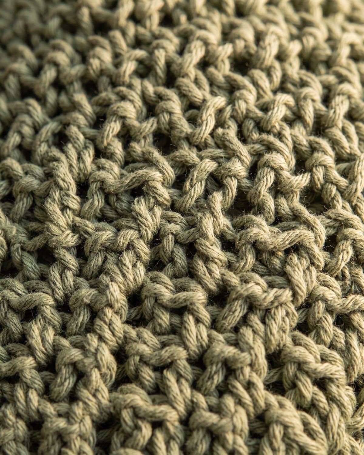 Close-up of the woven-looking texture of crochet moss stitch in sage green cotton yarn