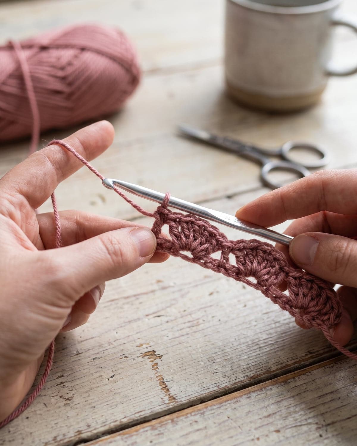 Hands crocheting the first row of shell stitch fans in dusty rose yarn
