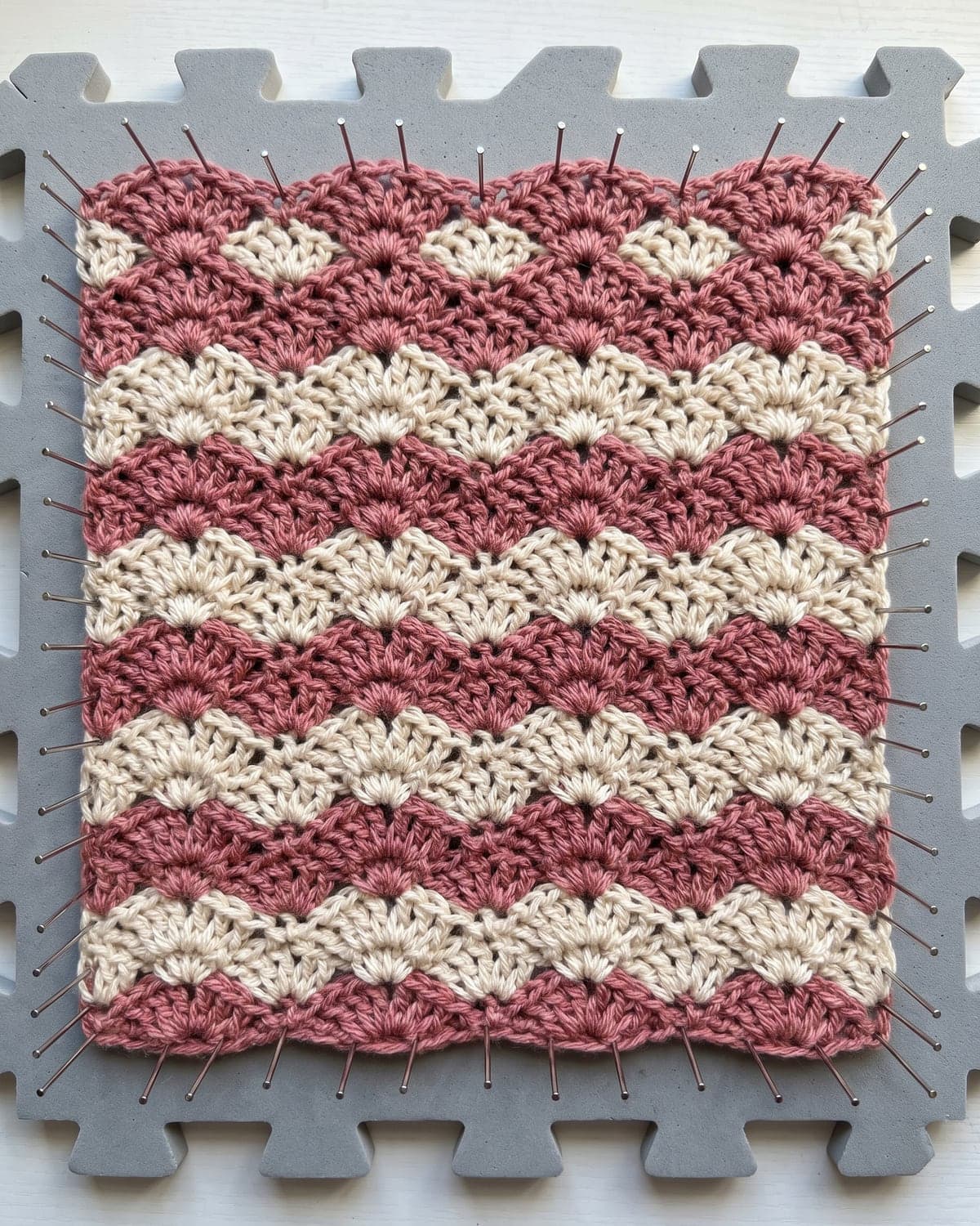 Striped crochet shell stitch swatch in dusty rose and cream pinned to a grey blocking mat