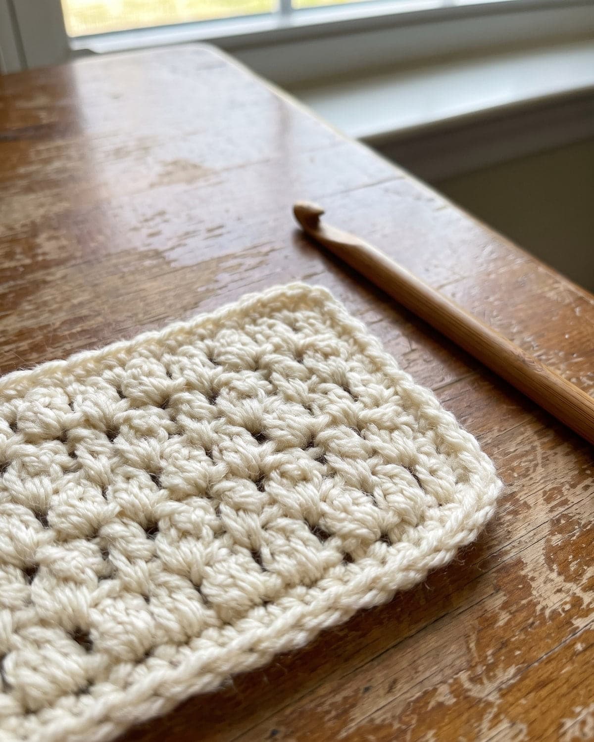 Close-up of a cream crochet swatch with a pebbled texture, with a wooden hook beside it
