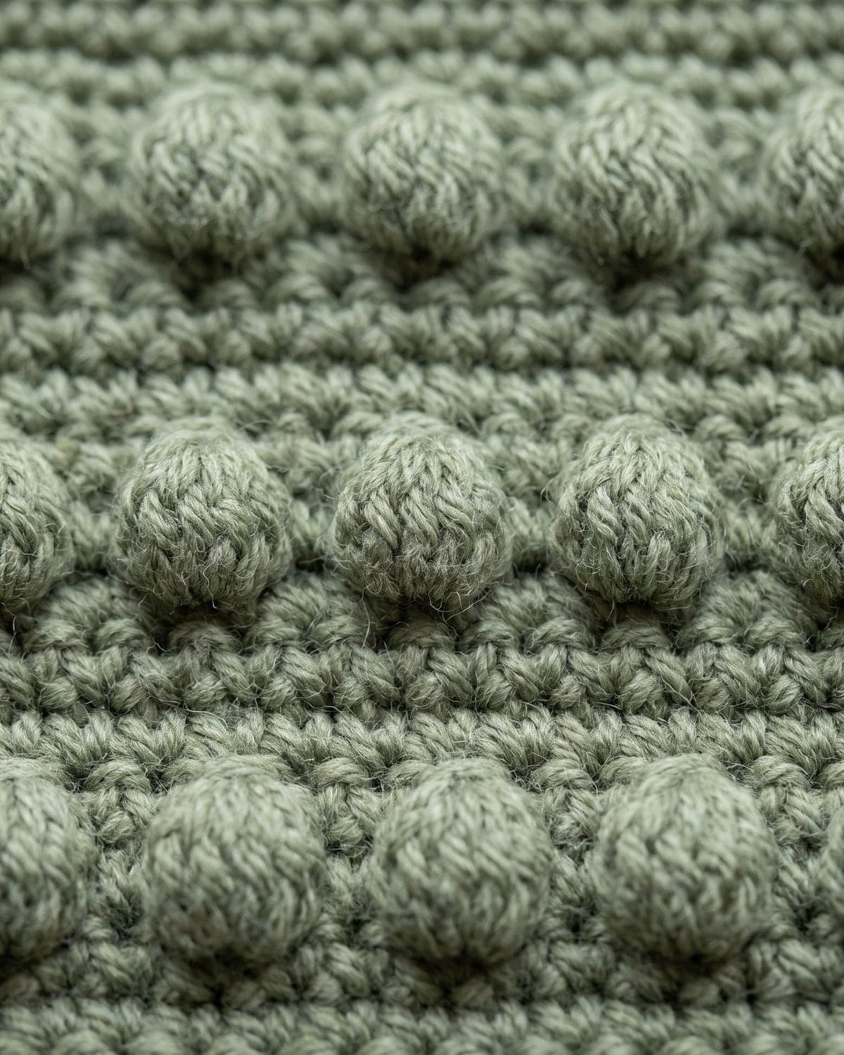 Close-up of sage green crochet fabric with rows of round raised bobbles