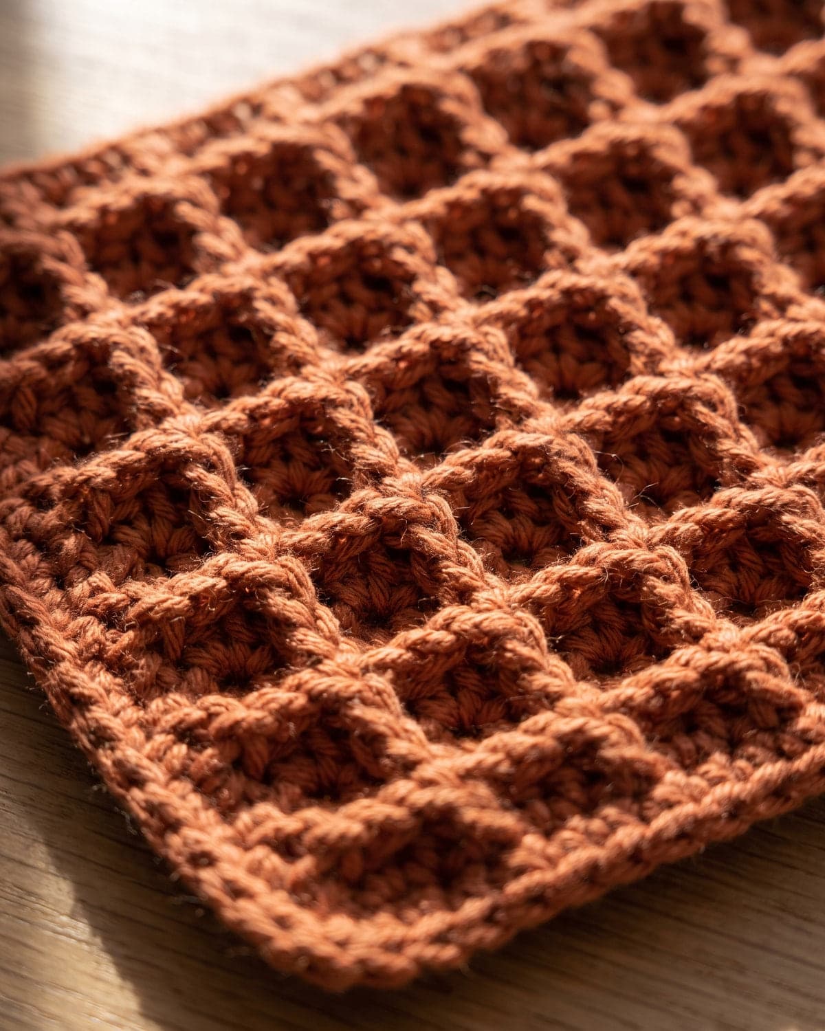 Close-up of a terracotta crochet swatch in waffle stitch with a deep grid of raised squares