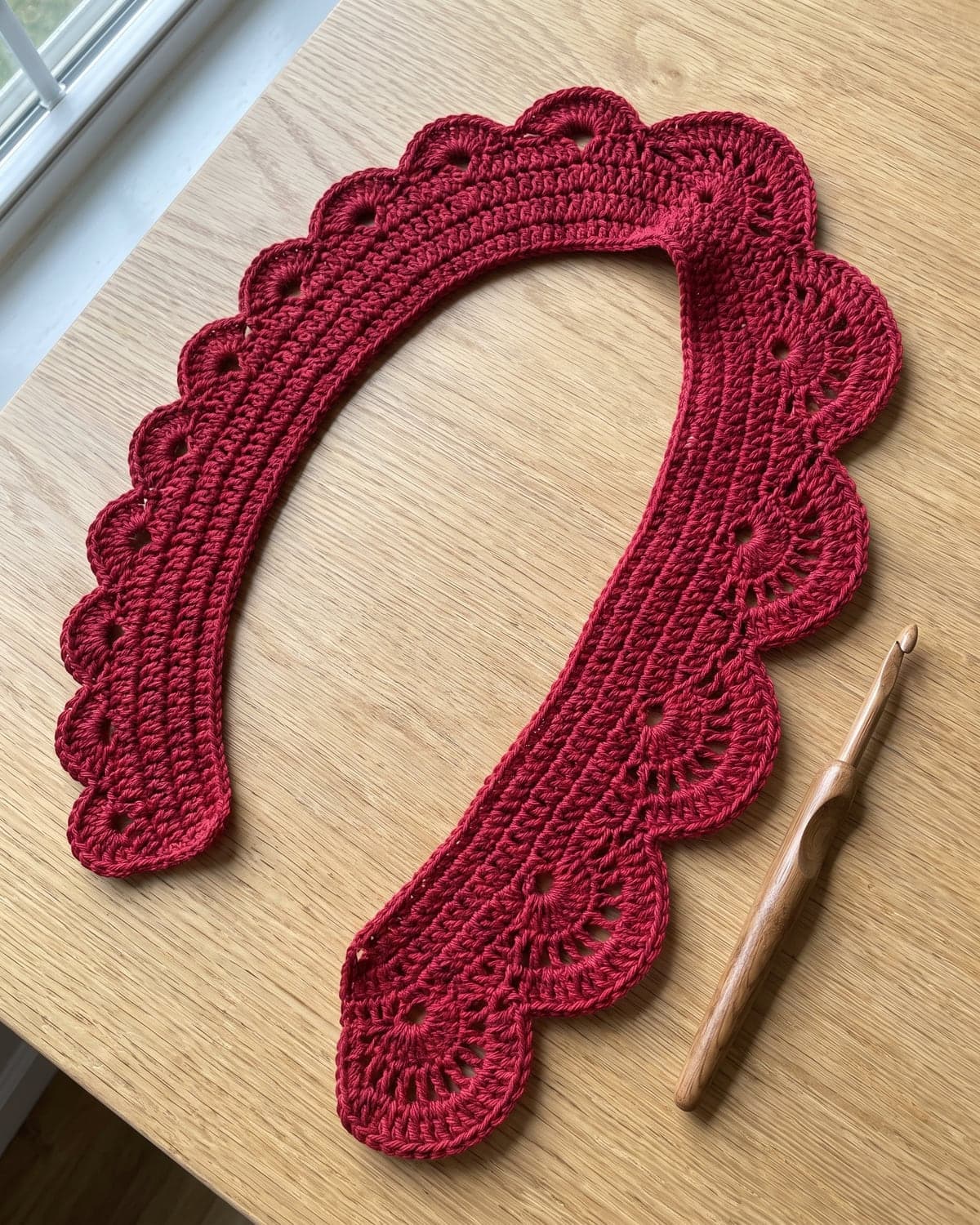 Long flat crochet strip in deep red yarn with a row of scalloped petals along its edge