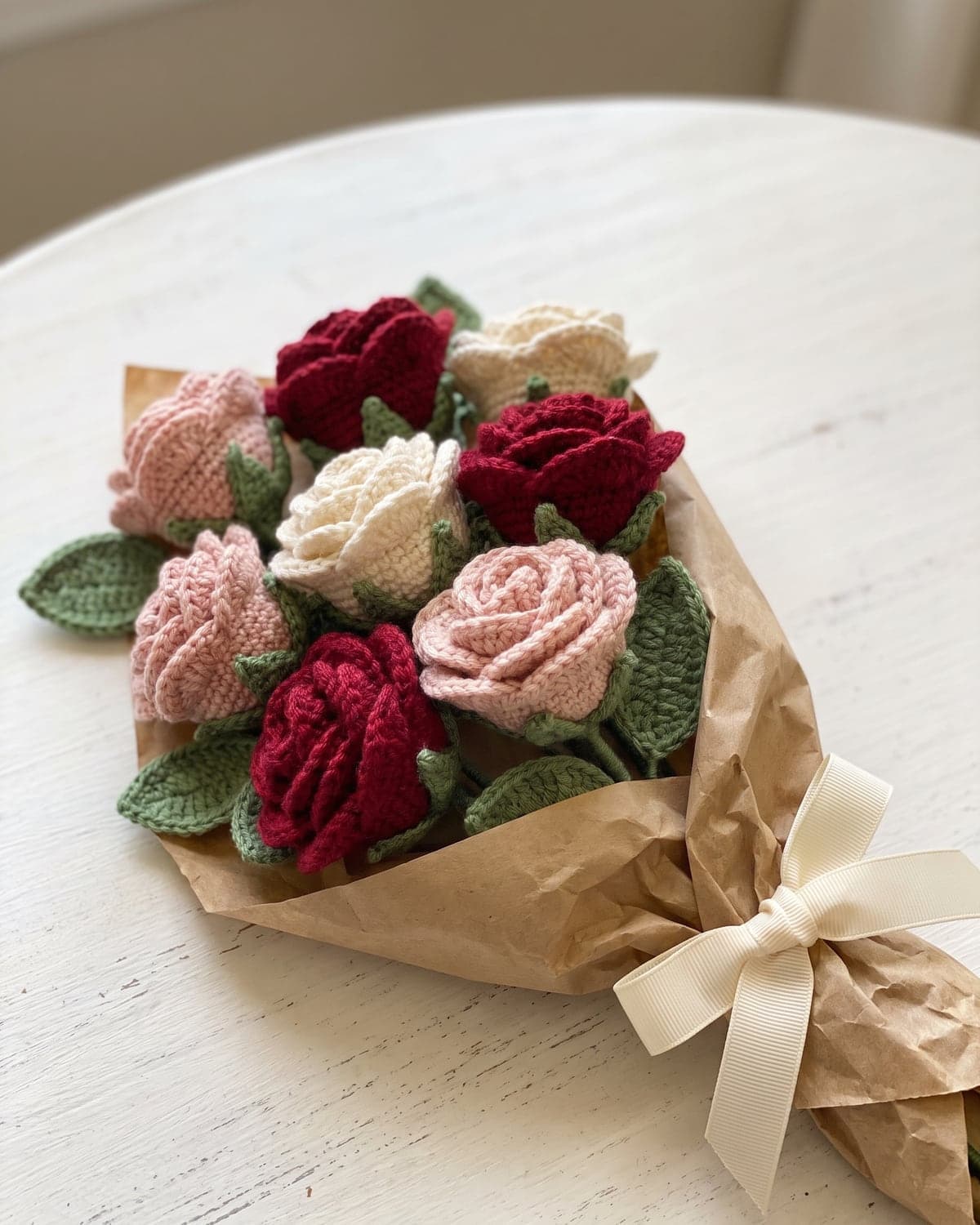 Bouquet of crochet roses in red, blush pink and cream wrapped in kraft paper with a cream ribbon