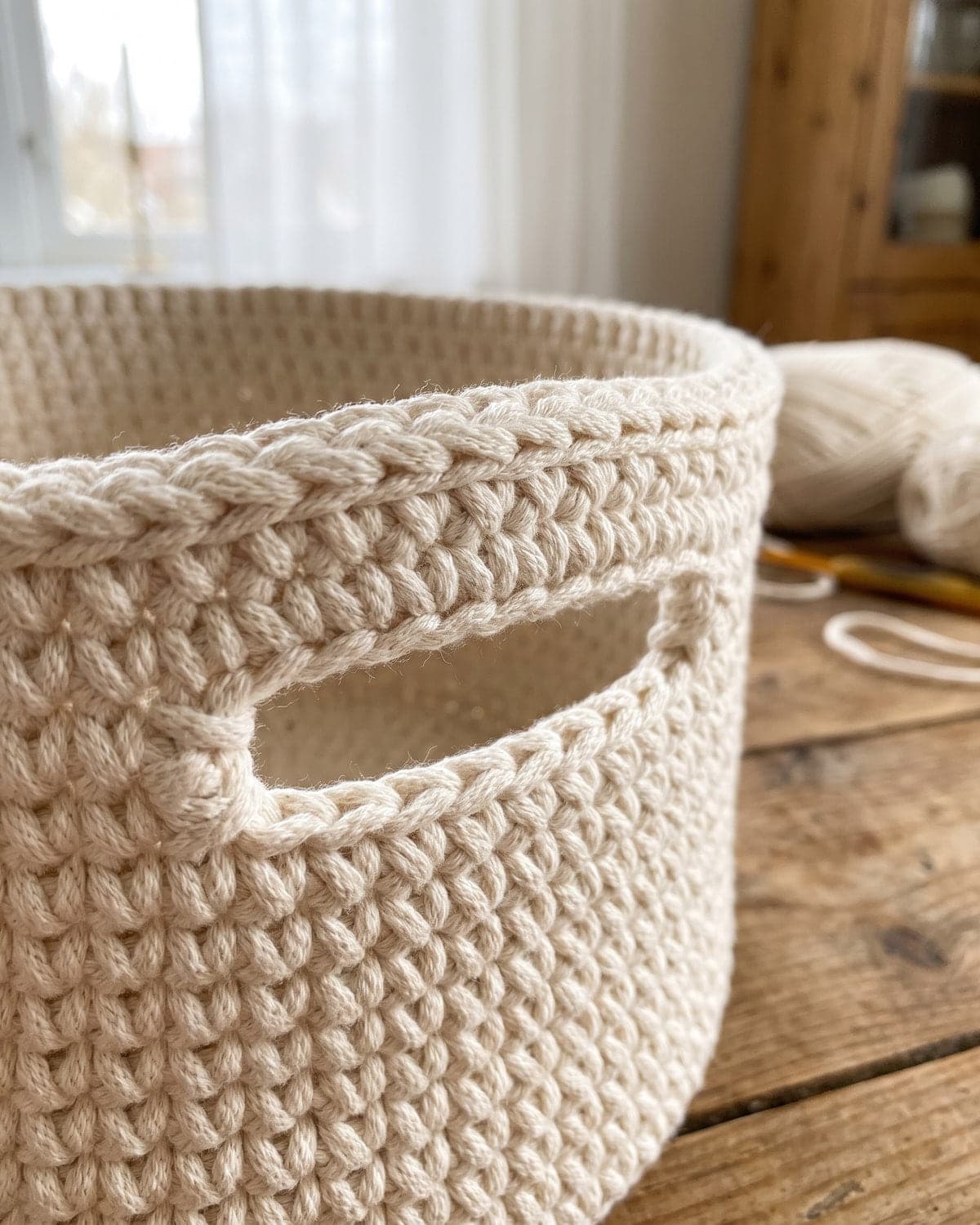 Close-up of a built-in handle opening below the rim of a cream crochet basket